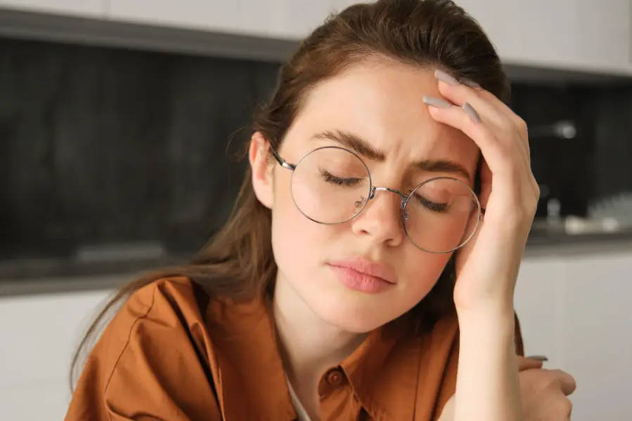 Portrait of tired young working woman in glasses holds hands on head suffers painful migraine has